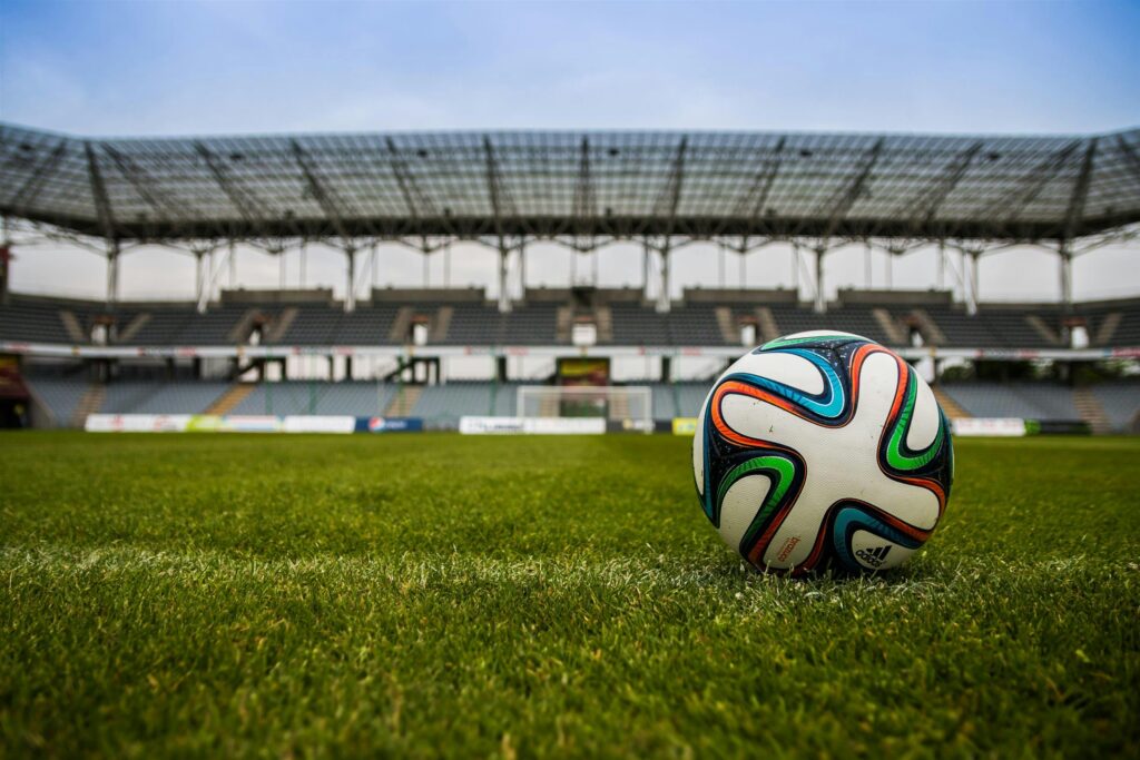Close-up of a soccer ball on a lush grass field with an empty stadium in the background.