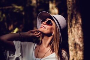 A fashionable woman in sunglasses and hat enjoying a sunny day outdoors, radiating confidence and joy.