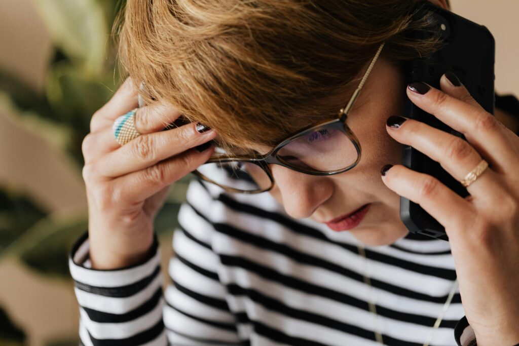 Focused woman with eyeglasses discussing work over a phone call, looking concerned and thoughtful.